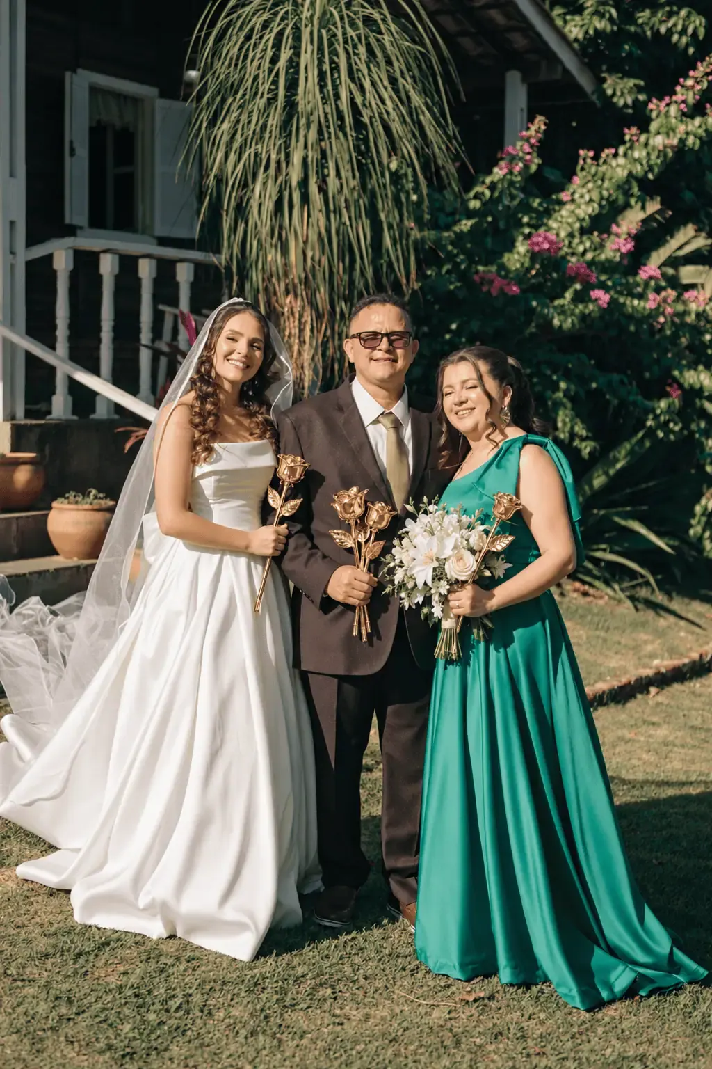 Bride, her father and a bridesmaid holding gold dipped roses in a garden, real roses dipped in 24K gold