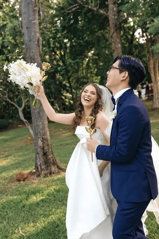 Bride raising her bouquet as the groom holds a gold dipped rose in a garden, the moments this gold dipped rose guide is written for