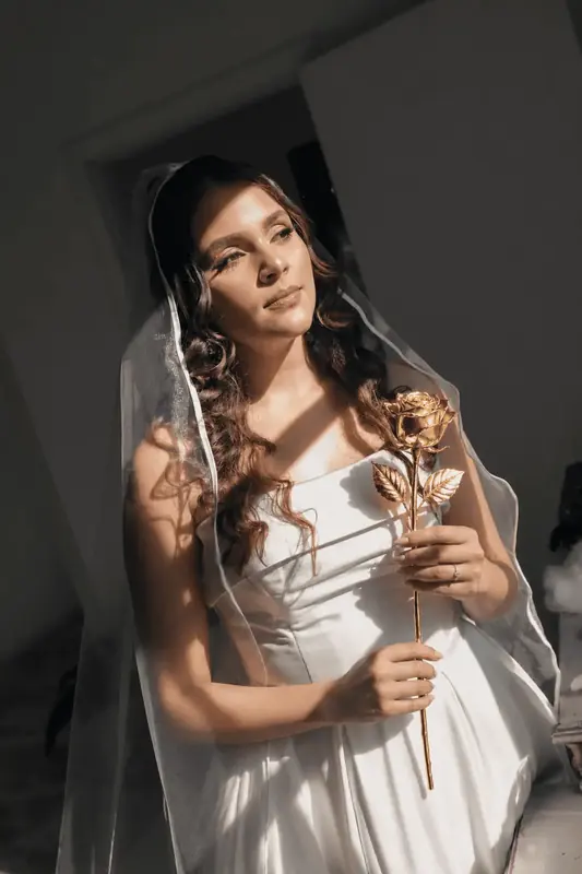 Bride holding a single gold dipped rose against a dark background, gift inspiration for the 24K Gold Majestic gold dipped rose (one real rose preserved in 24K gold, crystal glass dome, premium satin box)