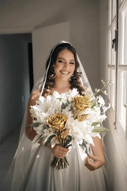 Smiling bride in a veil holding a gold dipped rose bouquet, real roses dipped in 24K gold