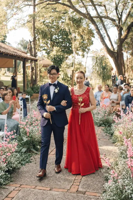 Couple walking the aisle, woman in a red dress, both holding gold dipped roses, gift inspiration for the Imperial Trinity Rouge gold dipped rose (3 real roses preserved in 24K gold, red crocodile leather)