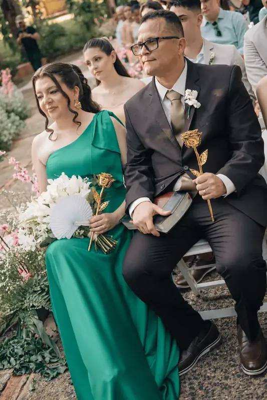 Guest in an emerald green dress holding a gold dipped rose next to a man in a dark suit, gold and green, the palette of the Imperial Trinity Emerald