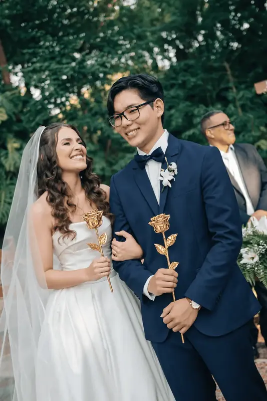 Groom walking with the bride while holding a 24K gold dipped rose, gift inspiration for the Imperial Trinity Noir gold dipped rose (3 real roses preserved in 24K gold, black crocodile leather)