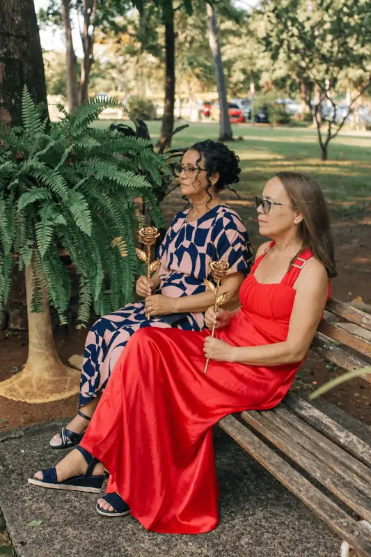 Two women on a garden bench holding gold dipped roses at a wedding, questions about choosing a gold dipped rose gift