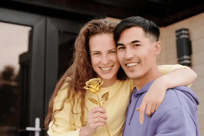 Happy couple embracing, the woman holding a gold dipped rose gift, the moment a gold dipped rose is given