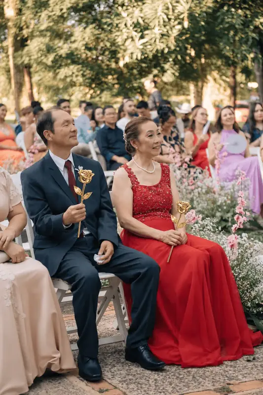 Wedding guests in a red dress and navy suit each holding a gold dipped rose, formal gift inspiration for the Imperial Trinity Noir